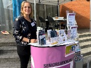 Seniorsamordnaren står vid sin lila monter på Hallstaviksdagen.